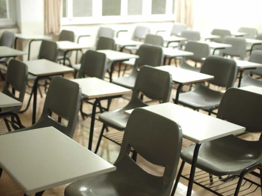 Rows of empty desks with sunlight streaming in from top right corner.